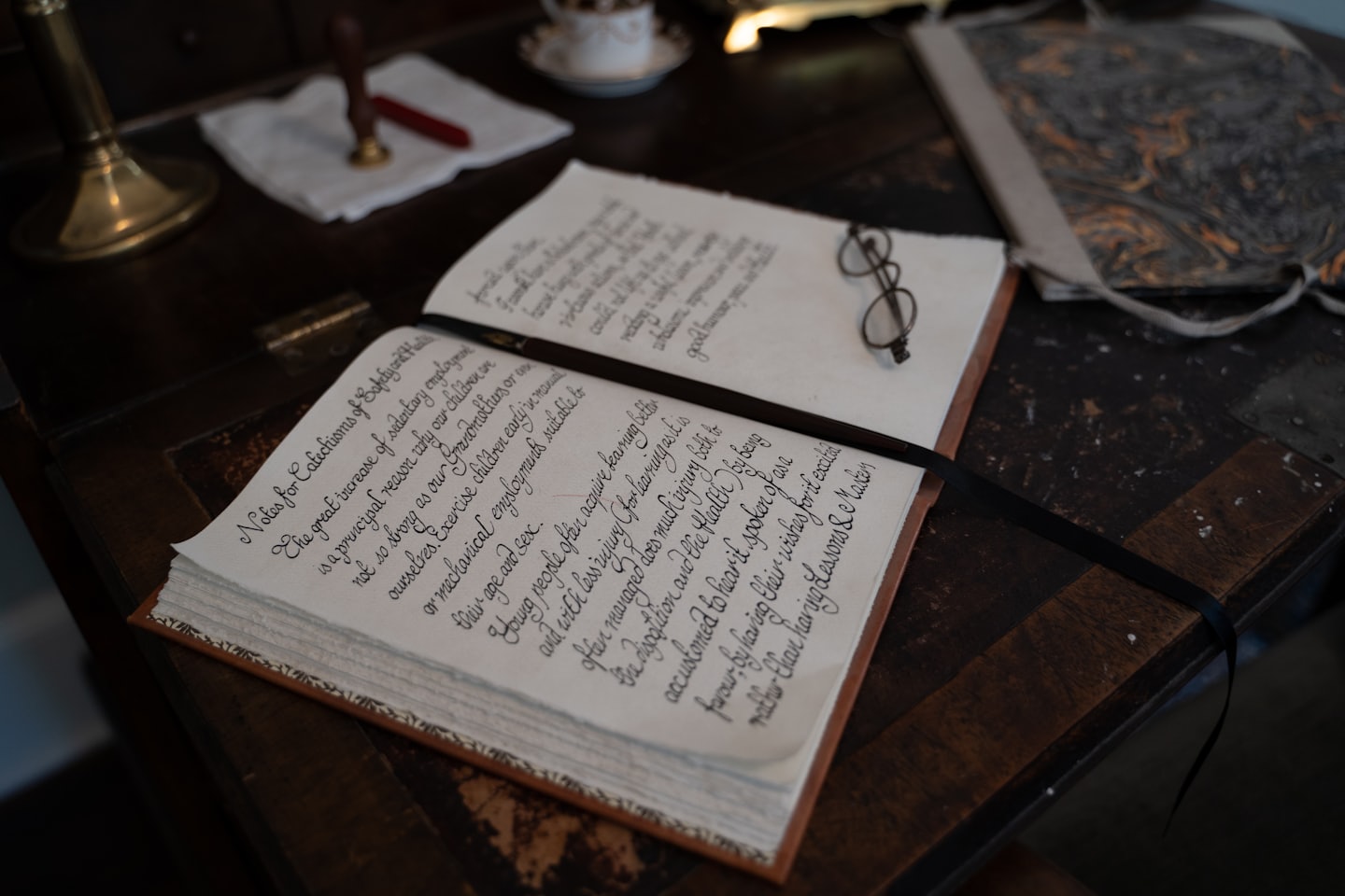 Wire spectacles rest on an open handwritten journal on a desk.
